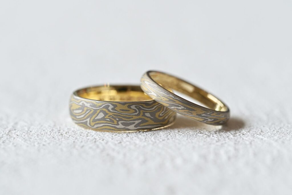 Matching Mokumegane wedding bands featuring a unique wood-grain pattern and different band widths