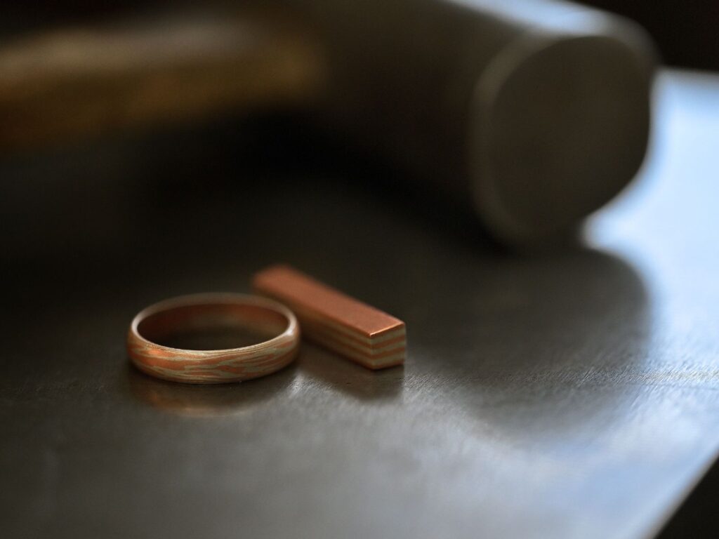 Finished Mokumegane ring and the layered metal stock from which its unique grain pattern is formed